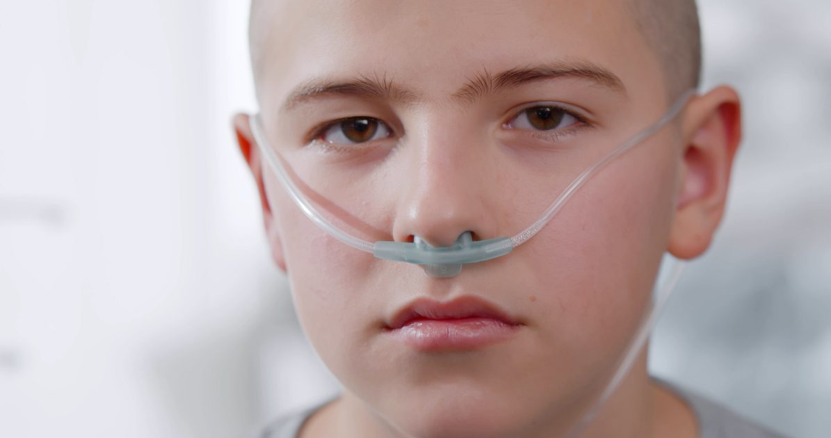 Close up portrait of sad sick boy with nasal cannula looking at camera in hospital. Teenage kid patient with cancer sitting in hospital ward having chemotherapy treatment.